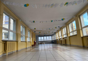 Na zdjęciu widać szkolny korytarz, pod sufitem zawieszone zostały sznurki, a na nich papierowe gołębie i serca z modlitwami i życzeniami.